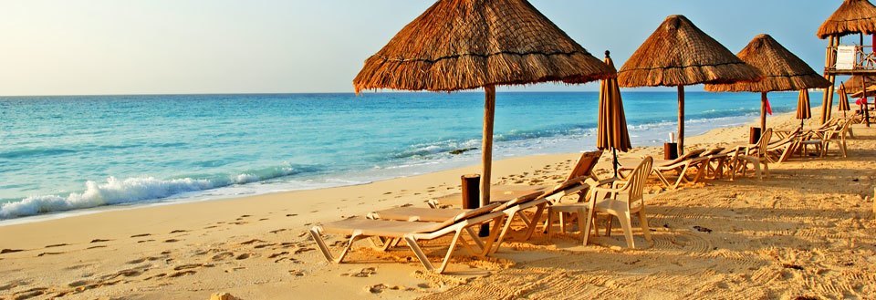 En solrik strand med stråparasoller og solsenger rettet mot det rolige turkise havet.