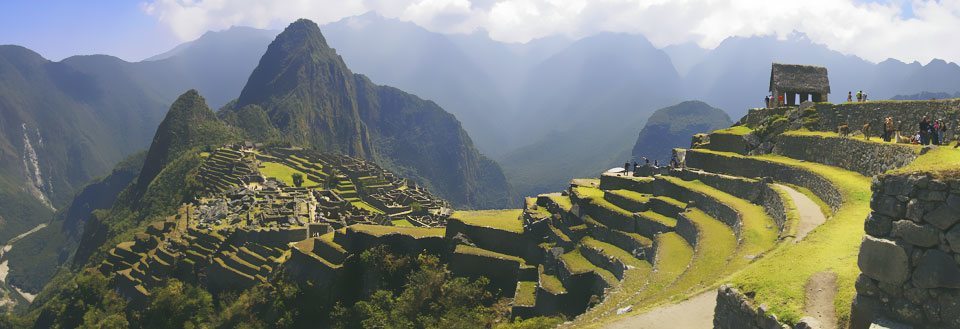 Panoramabilde av Machu Picchu med grønne terrasser mot en bakgrunn av tåkelagte fjell.