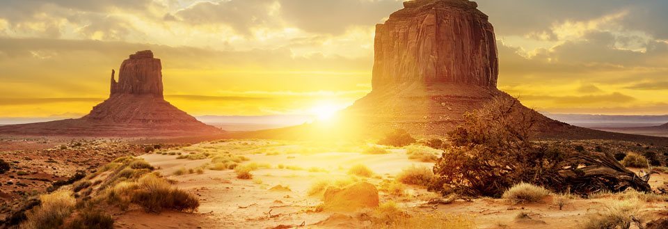 En ørken ved solnedgang med slående fjellformasjoner og et gyllent lys.