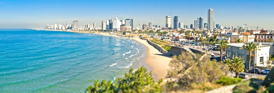 Panoramautsikt over en kystby med skyskrapere langs strandpromenaden og klart blått hav.