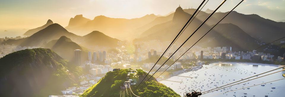 Bilde av en taubane med utsikt over Rio de Janeiro omgitt av åser og vann ved solnedgang.