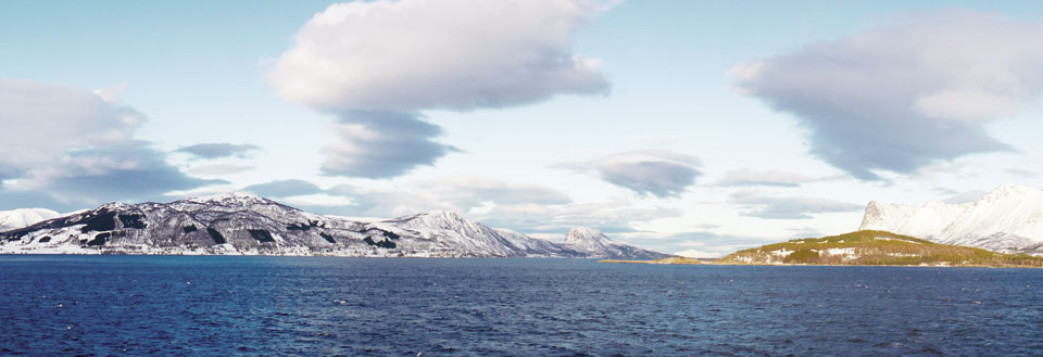 Vinterkyst med snødekte fjell og delvis skyet himmel.