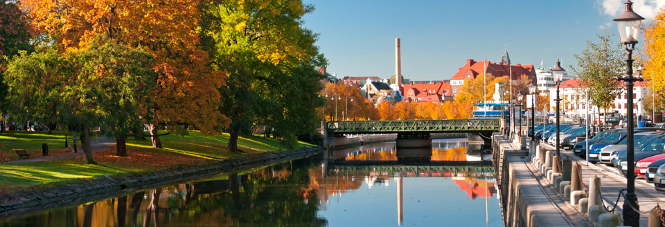 Rolig elv som renner gjennom en by med fargerike trær om høsten og klar blå himmel.