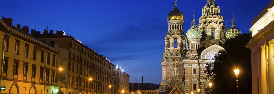 Kveldsbilde av en gate med historiske bygninger og en fargerik katedral i bakgrunnen.