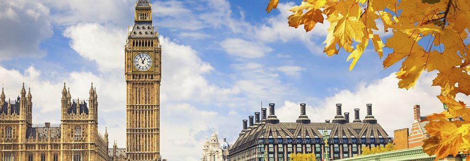 Big Ben og Westminsterpalasset i London, omgitt av gyldne høstblader på en solrik dag.