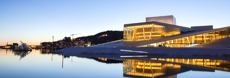 Moderne bygning reflekteres i vannet i skumringen, under en klar himmel med tent vinduer.