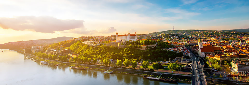 Panoramautsikt over en by ved en elv i solnedgangen, med historiske byggverk og en bro.