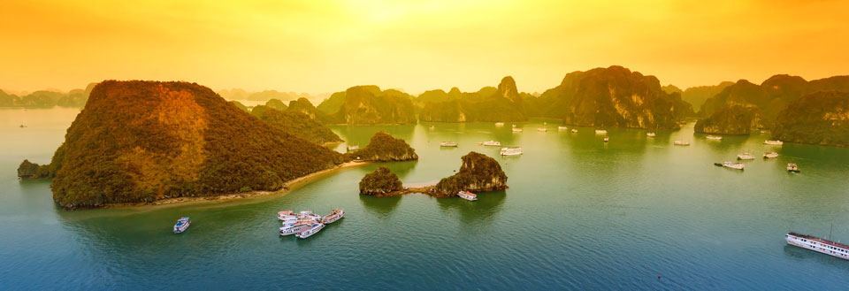 Dramatisk solnedgang over Halong Bay med kalksteinøyer og seilbåter.