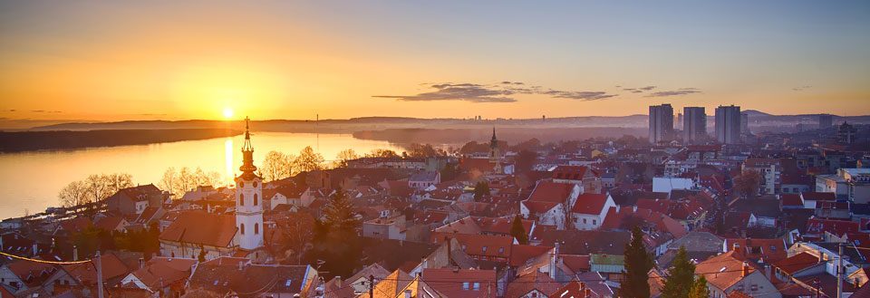 By ved solnedgang, med silhuett av en kirke og moderne bygninger i bakgrunnen.