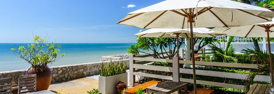 Strandterrasse er innbydende med oppslåtte parasoller, havutsikt, potteplanter og tre møbler.