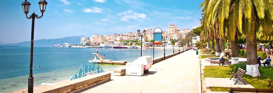 Solrik promenade i Albania med palmer langs sjøkanten og folk, som slapper av.