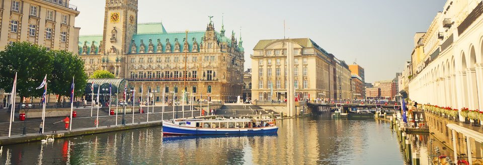 Panoramautsikt over en kanal i en by, omgitt av bygninger, en båt og flagg.