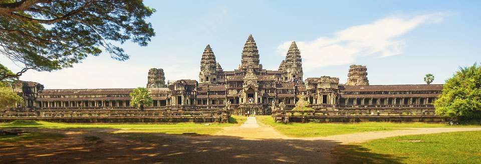 De majestetiske ruinene av Angkor Wat i Kambodsja, omgitt av grønne trær og en klar himmel.